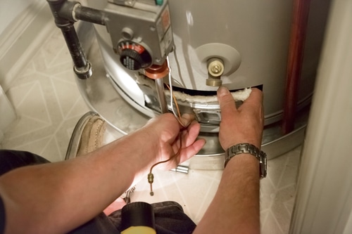A bottom view of man reaching at the bottom of a leaking water heater 