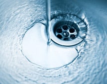 Water pouring from metal sink faucet into drain.