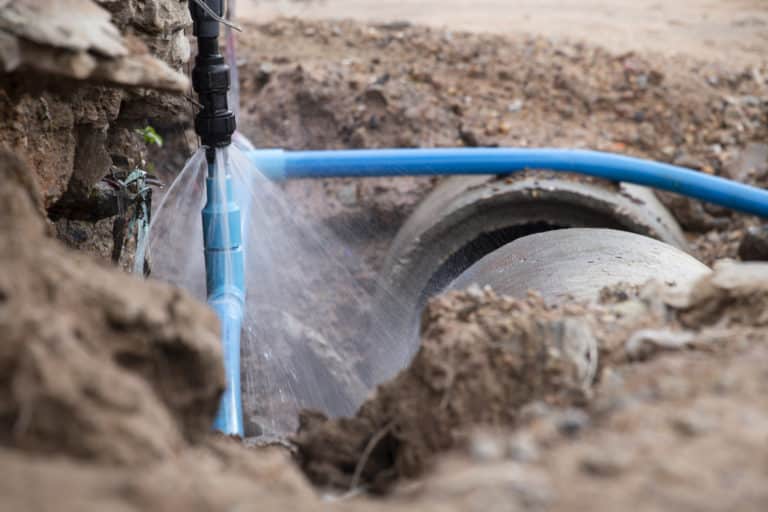 Underground burst pipe in blue next to a sewer line with soil in the background